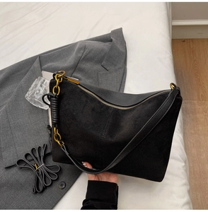 Close-up of black suede and leather bag showing golden zipper and chain detail
