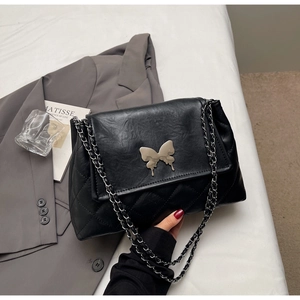 Détail d'un sac porté épaule noir matelassé avec fermoir papillon argenté et chaîne