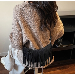 Detail view of a black fringe crescent bag worn with a brown knit sweater and white pants