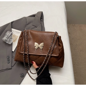 Détail d'un sac matelassé marron avec fermoir papillon argenté et bandoulière chaîne