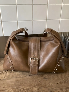 Brown vintage faux leather tote bag with silver rivets and metal buckle on wooden table
