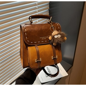 Dettaglio zaino vintage in ecopelle marrone con cuciture a contrasto e ciondolo peluche