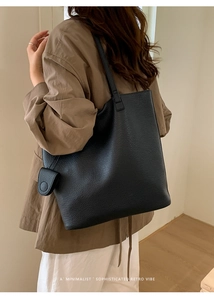Detail of a black pebbled leather tote bag with a small matching accessory on a model