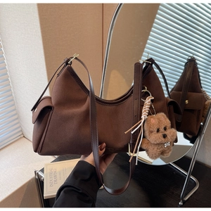 Dettaglio borsa a spalla in pelle scamosciata marrone scuro con tasca laterale e ciondolo