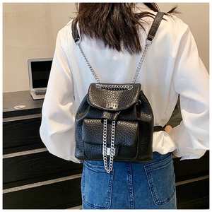 Detail of black textured leather backpack with metal chain straps and turn-lock closure