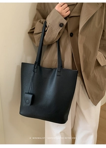 Minimalist black tote bag with litchi texture and long straps worn with an autumn trench coat