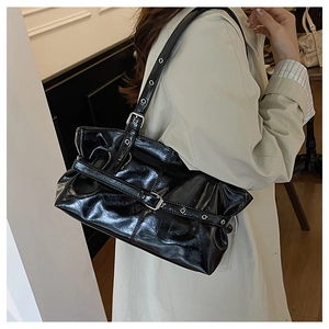 Detail of black glossy shoulder bag with silver eyelets shown on light trench coat