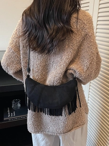 Minimalist black suede crescent bag with tassels and shoulder strap on model back