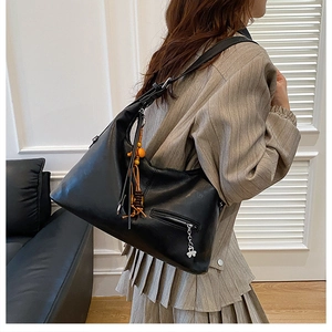 Vue détaillée du grand sac cabas noir avec breloque trèfle et pompon perlé sur le côté