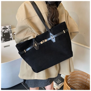 Detail of a black suede tote bag with a gold metal clasp shown in a lifestyle setting