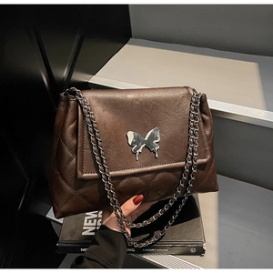 Détail d'un sac matelassé marron avec fermoir papillon argenté et bandoulière chaîne