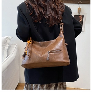 Vue détaillée d'un sac cabas marron en demi-lune avec glands et pendentif fleur