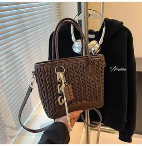 Detail of dark brown tote bag with woven texture, chocolate charm and striped rope accessory