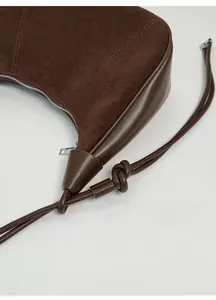 Detail of brown suede dumpling bag featuring adjustable knotted strap and silver zipper closure