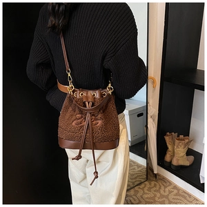 Brown faux shearling bucket bag with drawstring and leather trim worn crossbody by model