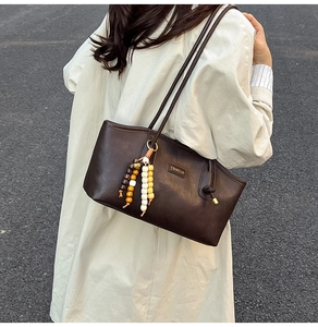 Detail view of a vintage dark brown tote bag with beaded tassel on a beige trench coat