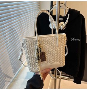 Close-up of beige woven bucket bag with chocolate charm and leather reinforced bottom