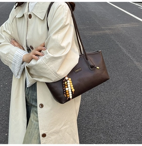 Detail of dark brown leather tote bag with metallic logo and colorful wooden bead charms
