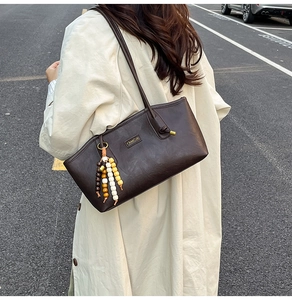 Close-up of deep brown leather tote bag with colorful bead charm on a trench coat model