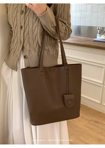 Detail of brown litchi pattern leather tote bag with a minimalist round pendant charm