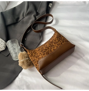 Detail of leopard print crossbody bag with brown leather accents and plush charm