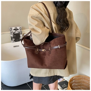 Detail of suede tote bag featuring dark brown leather straps and gold metal lock buckle