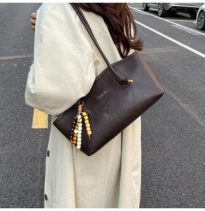 Detail of dark brown vintage leather tote with decorative beaded tassel and metal logo