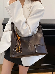 Sac hobo rétro marron foncé grande capacité avec pompon porté sur un costume blanc