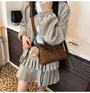 Detailed shot of leopard print crossbody bag with plush puppy charm and brown leather straps