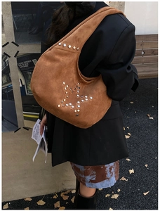 Close-up of brown suede tote bag with metallic rivet star pattern in outdoor setting