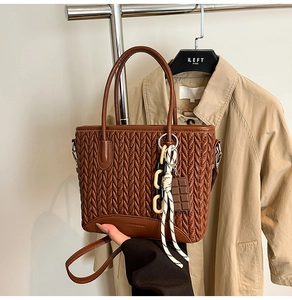 Close-up of brown quilted bucket bag with V-shaped texture and decorative pendants