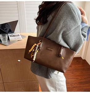 Detail of a dark brown leather tote bag with colorful wooden beads and brand logo
