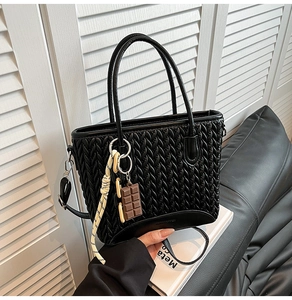 Detail of black quilted woven texture bucket bag with chocolate charm and crossbody strap