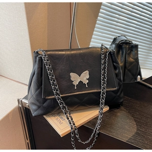 Gros plan d'un sac bandoulière noir matelassé avec ornement papillon argenté et bandoulière chaîne