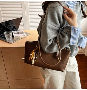 Detail of dark brown leather tote bag with pebble texture and colorful beaded tassel charm