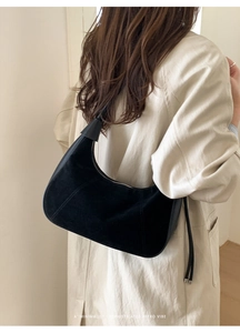 Detail of a black matte suede hobo bag worn with a chic trench coat for a retro vibe