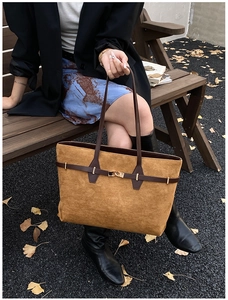Detail of ochre suede tote bag with brown leather straps and gold buckle on a park bench