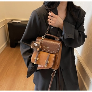 Dettaglio di uno zaino vintage in pelle marrone con cuciture a contrasto e ciondolo