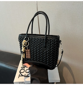 Close-up of black woven texture tote bag with chocolate charm on white books