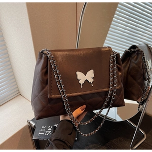 Détail d'un sac matelassé marron avec ornement papillon argenté sur un miroir