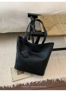 Detailed close-up of a black lychee texture leather tote bag on a stylish woven chair