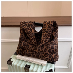 Detail view of the leopard print tote bag resting on a suitcase in a minimalist setting