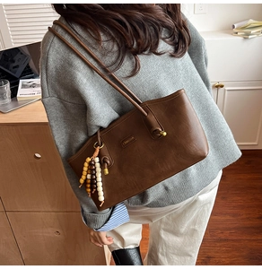 Detail of deep brown vintage tote bag with metal logo and wooden bead charm accessory