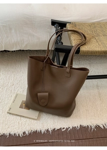 Close-up of brown lychee grain leather tote bag with round charm on a cream rug