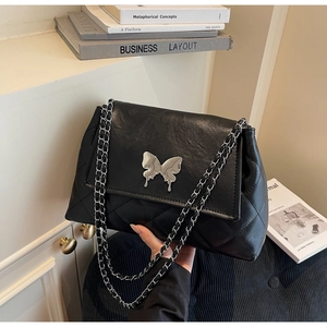 Détail de la texture en cuir noir matelassé et de la boucle papillon argentée sur le sac
