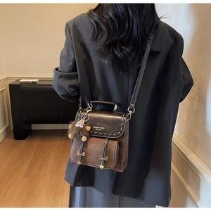 Dettaglio di uno zaino vintage in pelle marrone con cuciture bianche e ciondolo di peluche