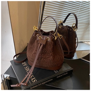 Detail of dark brown faux fur bucket bag with leather handle and gold hardware on books
