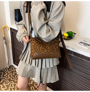 Detail of leopard print handbag featuring brown leather trim and adjustable shoulder strap