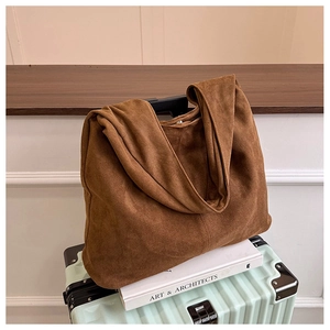 Brown suede tote bag on books and mint luggage in a warm minimalist interior