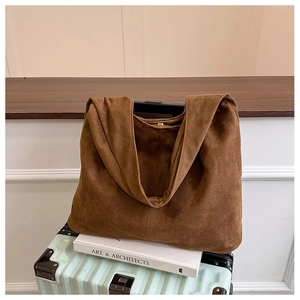 Brown suede tote bag placed on a suitcase and books showing minimalist vintage urban style